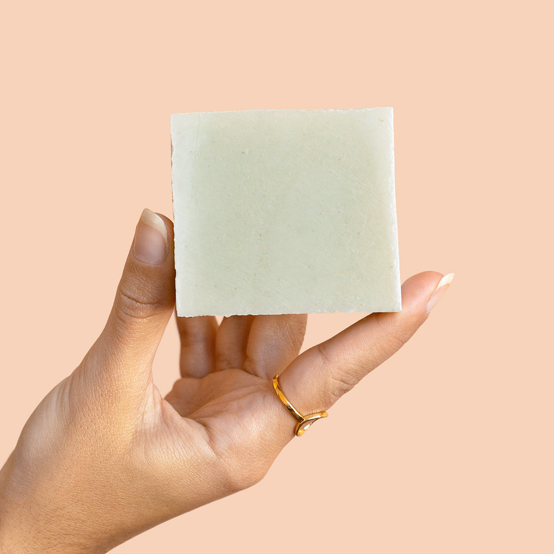Hand holding a light green body soap bar against a beige background