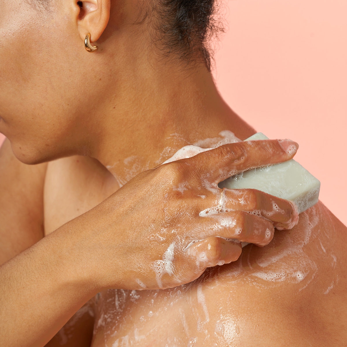 Person scrubbing their shoulder with a bar of soap against a pink background