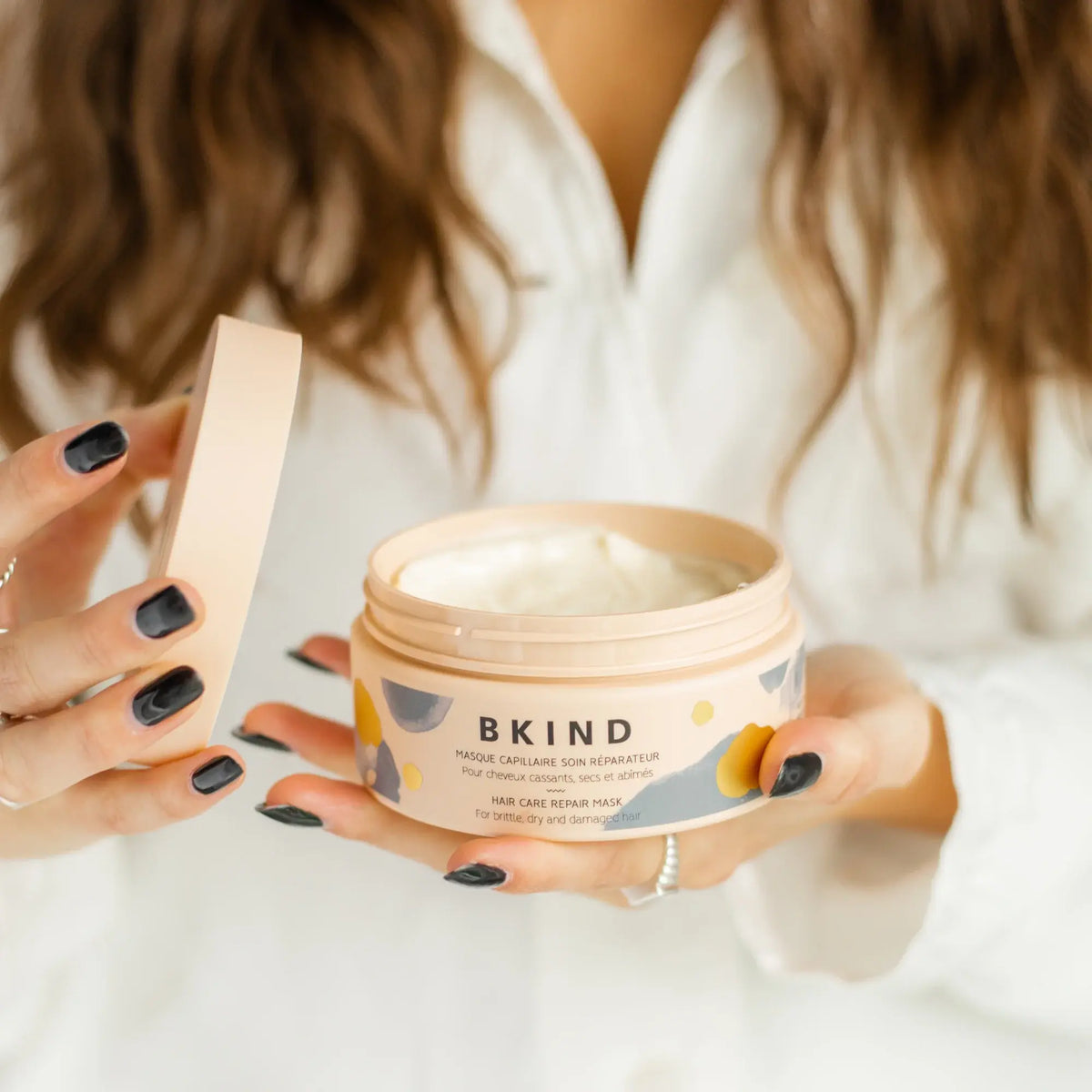 Person holding a jar of BKIND hair care product with a white background