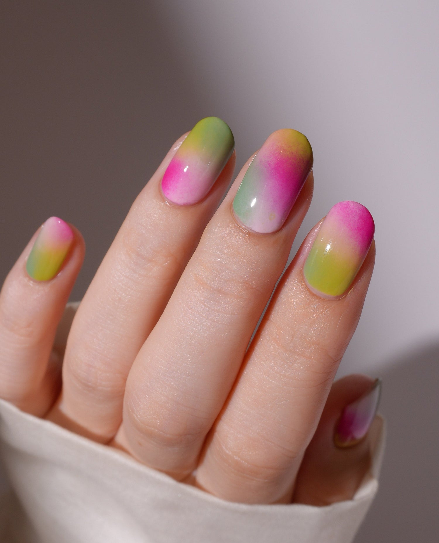 Close-up of a hand with colorful gradient nails on a neutral background