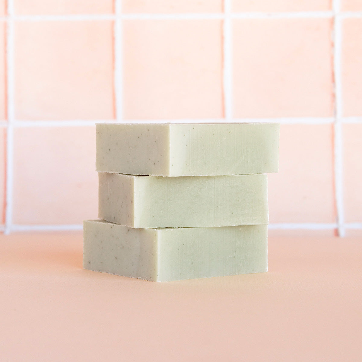 Three bars of soap stacked on a pink tiled bathroom wall.
