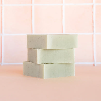 Three bars of soap stacked on a pink tiled bathroom wall.