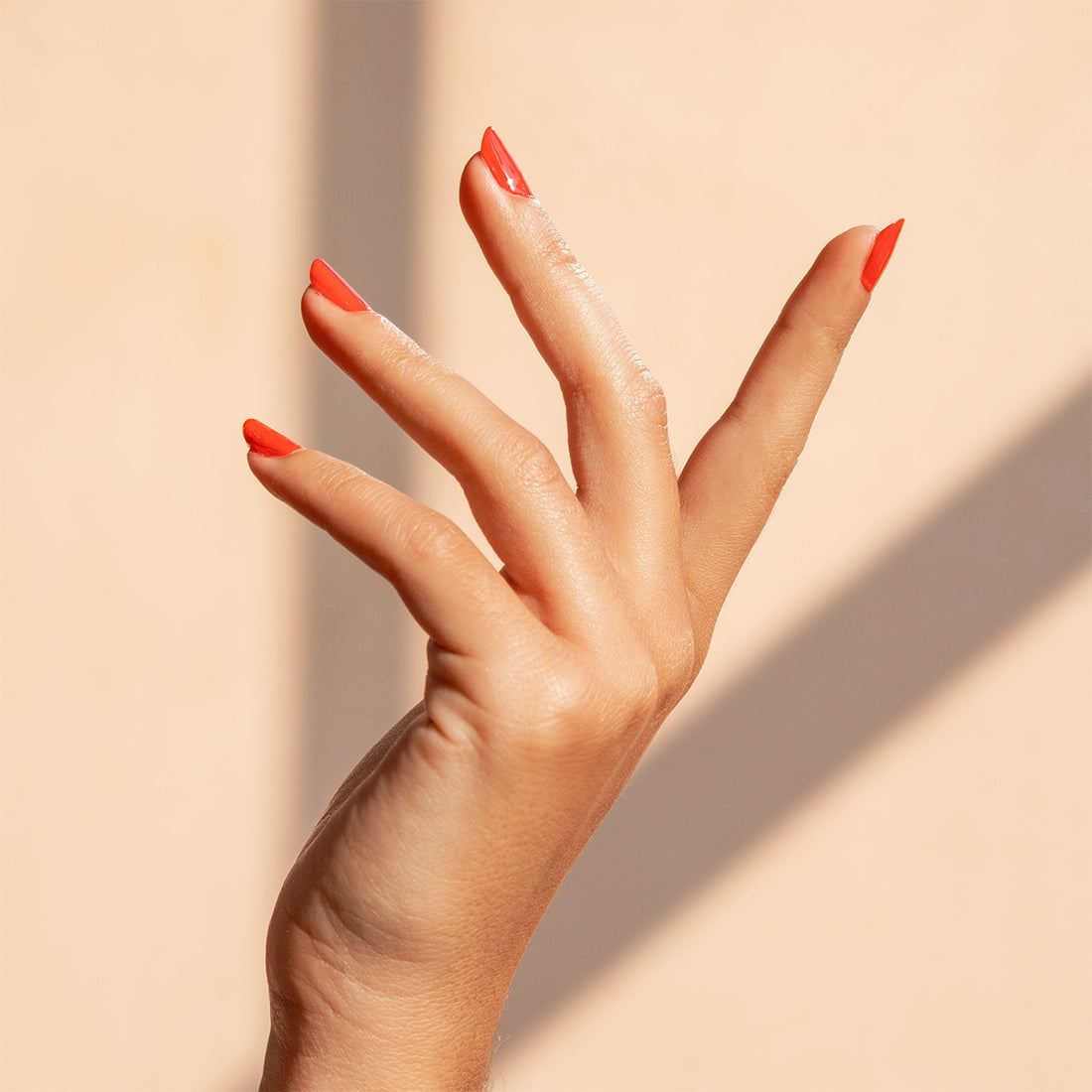 Hand with red nail polish on a beige background