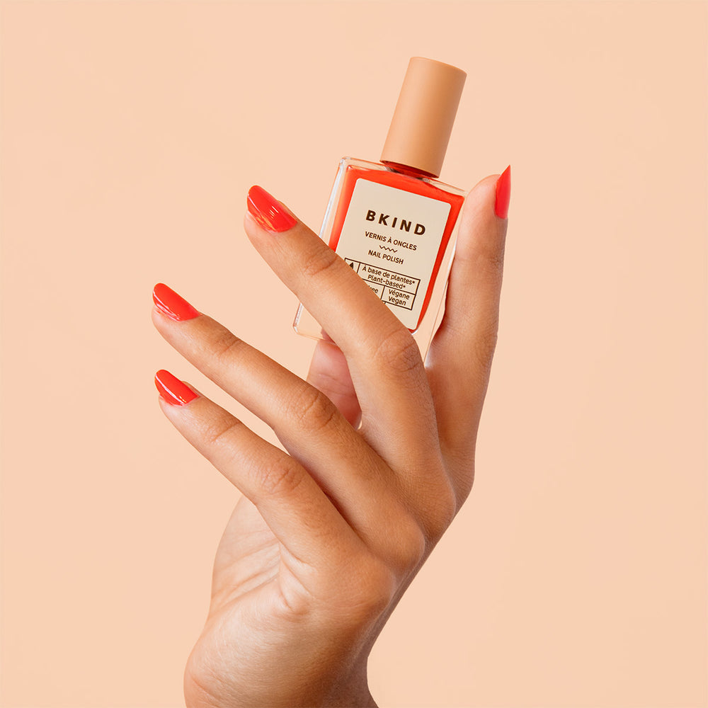 Hand holding a bottle of BKIND nail polish against a beige background