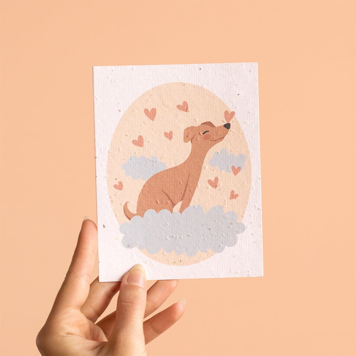 Hand holding a card with a dog illustration and heart shapes on a beige background
