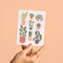 Hand holding a card with plant designs on a beige background