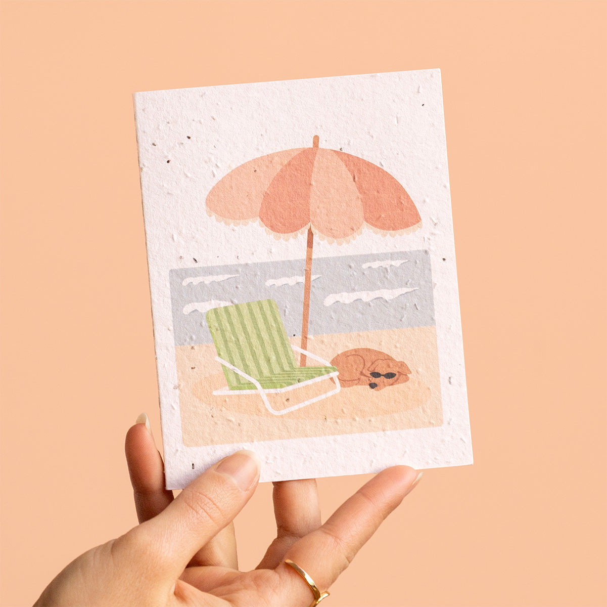 Hand holding a card with a beach scene illustration on a beige background