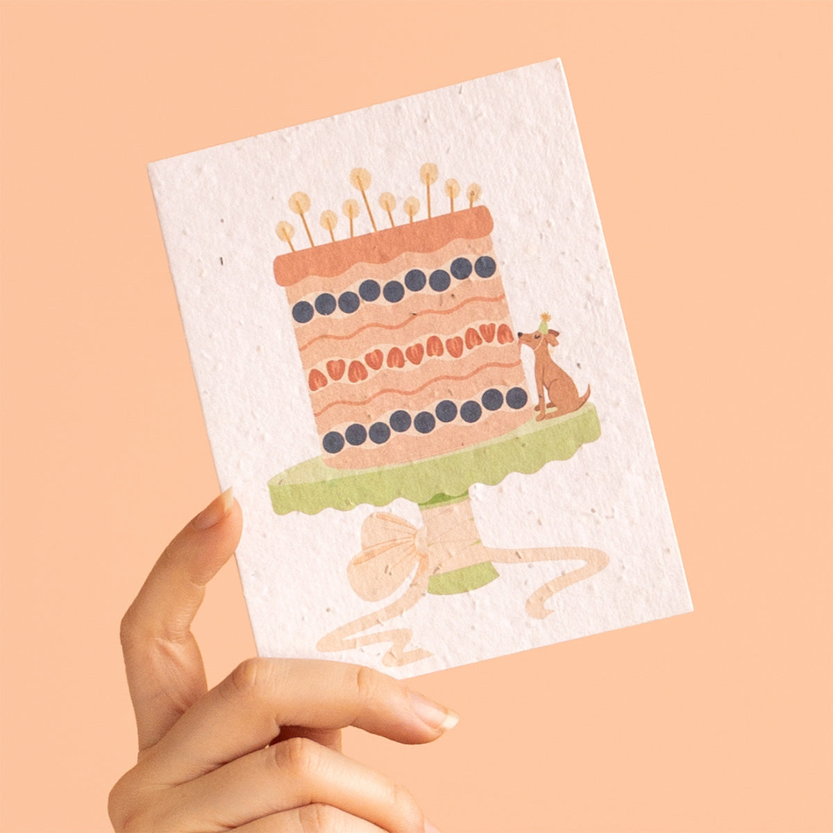 Hand holding a card with a cake illustration on a peach background