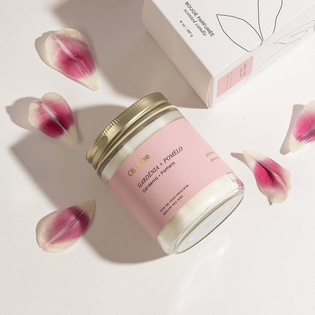 Candle with pink label and gold lid on a light surface with petals around