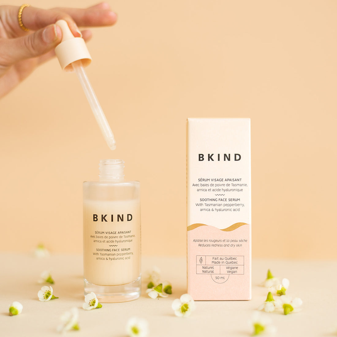 BKIND serum bottle and packaging with a hand holding a dropper on a beige background.