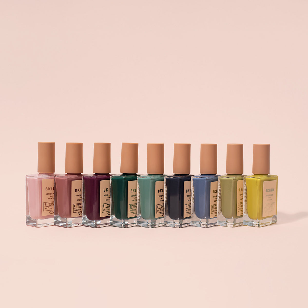 Row of nail polish bottles with beige caps on a light pink background