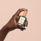 Hand holding a green bottle with a beige cap against a beige background