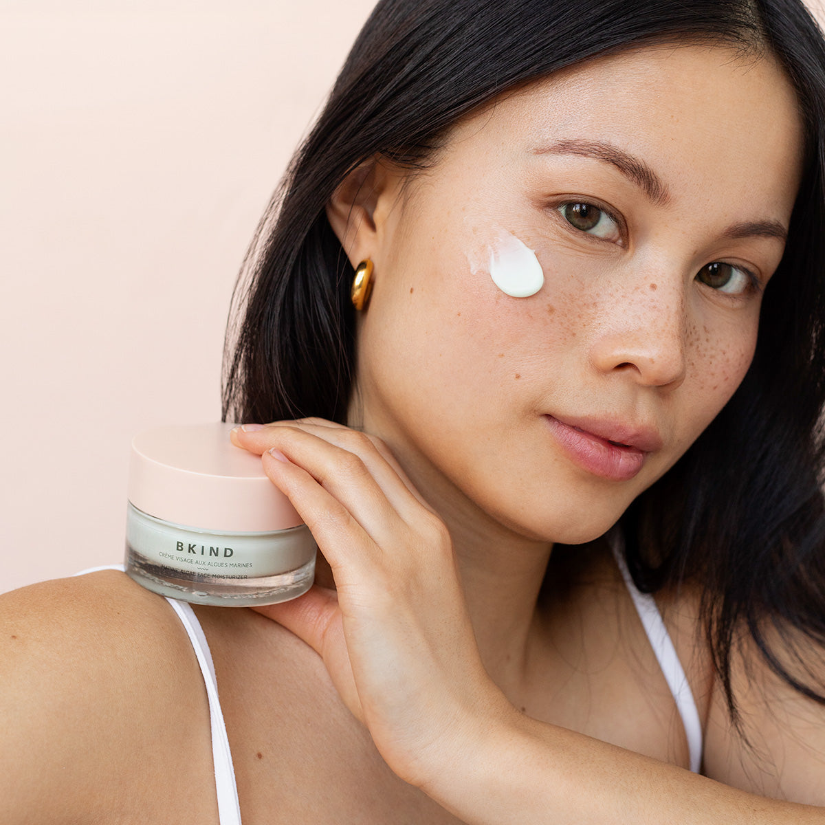 Model holding the Marine Algae face moisturizer with a swoosh of cream on her face